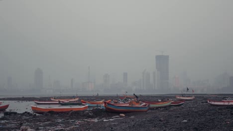 Beached,-colourful-fishing-boats-on-the-Mumbai-shore-with-large-buildings-in-the-background