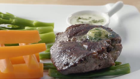 Close-Shot-of-Garlic-and-Herb-Butter-Melting-on-a-Steak-With-Vegetables-on-a-White-Plate