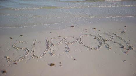 Turning-shot-of-SUPPORT-written-in-the-sand-on-a-beach