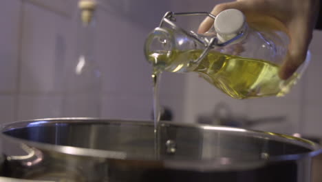 Close-handheld-shot-as-pouring-olive,-or-sunflower-oil-from-a-bottle-in-to-a-pot-in-the-kitchen