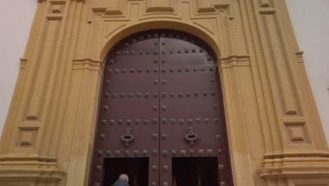 Tilt-Down,-Spanish-church-entrance-with-man-standing-in-doorway,-Seville,-Spain