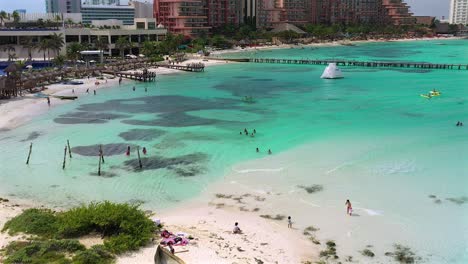 Aerial-Drone-footage-of-people-enjoying-their-day-in-the-clear-blue-ocean,-swimming-and-kayaking,-at-the-beach,-behind-the-Hyatt-Ziva-in-Cancun,-Mexico