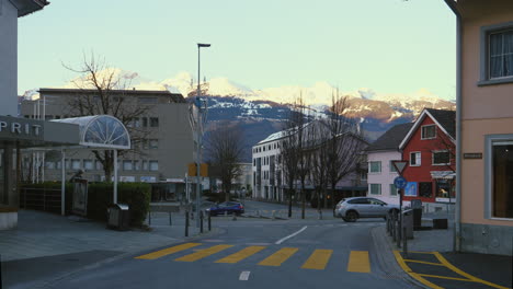 Vaduz-Liechtenstein,-Cars-going-around-a-roundabout-with-visible-snowy-mountains-in-the-background
