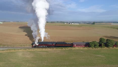 Aerial-side-by-side-view-of-a-N-W-steam-engine-blowing-steam-in-countryside-getting-ready-to-pull-passenger-cars-with-view-of-farmlands