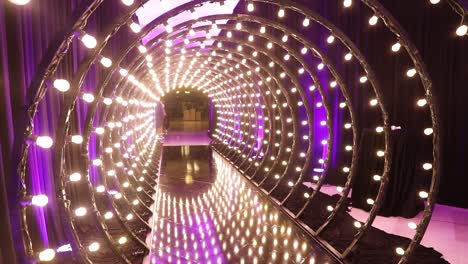 Tunnel-of-light-bulbs-in-a-perspective-pan-view-with-pink-violet-colors,-abstract-copy-space