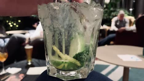 Person-stirring-and-pushing-lime-of-mojito-cocktail-in-hotel-bar,close-up