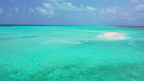 Paradise-scenery-of-calm-clear-water-on-turquoise-color-around-a-tiny-white-sandy-pile-under-bright-cloudy-sky-in-Maldives
