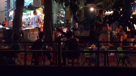 Wide-Exterior-Shot-of-People-Sitting-on-Small-Plastic-Chairs-and-Talking-in-a-Small-Out-Door-Restaurant-wile-Others-Are-Busy-In-The-Background-in-the-Night-Time