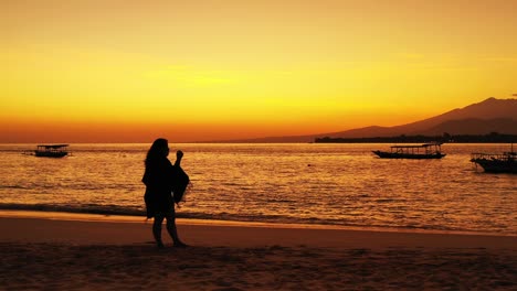 Woman-standing-in-the-sand-of-a-beach-watching-the-golden-glow-of-the-afternoon-sun-setting