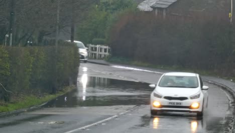 Vehicles-driving-along-rainy-stormy-flash-flooded-road-corner-bend-UK