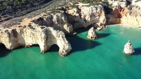 Rock-eroded-arch-formations-in-Marinha-Beach-south-of-Portugal,-Aerial-pan-right-shot