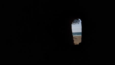 Abstract-view-of-beach-and-ocean-through-a-darkened-cave-opening