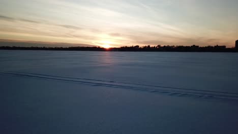 Sunset-frozen-lake,-camera-going-forward-above-snow