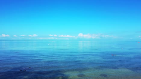 Peaceful-seascape-with-calm-shallow-lagoon-where-people-swim-and-white-clouds-rising-from-horizon-to-bright-blue-sky-in-Malaysia