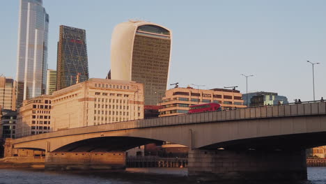 Red-British-bus-driving-over-bridge-towards-corporate-office-tower-buildings