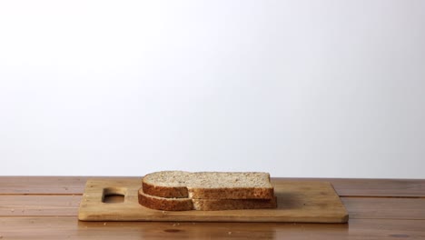 Slices-of-whole-wheat-bread-falling-down-on-top-of-each-other-one-at-a-time-on-a-wooden-cutting-board-against-a-white-background