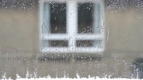 Close-up-of-melting-sleet-on-a-window-while-it-rains-outside