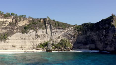 Sandy-Diamond-Beach-in-Nusa-Penida-island-Indonesia-with-rock-walls-behind,-Aerial-dolly-out-reveal-shot