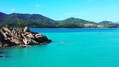 Blue-azure-sea-on-beautiful-rocky-coastline-of-tropical-island-with-green-hills-under-bright-blue-sky-in-Vietnam