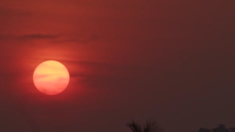 Large-red-sun-slowly-going-under-during-sunset,-close-up
