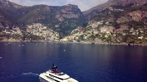 Amalfi-coast-with-superyacht-anchored-nearby-on-deep-blue-waters-of-the-Mediterranean-sea,-Aerial-flyover-reveal-shot