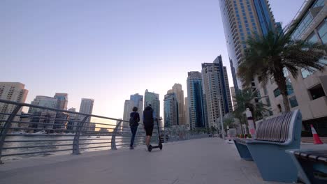 Dubai-Marina-Walk,-pedestrians-walking-along-the-waterfront-walkway-at-sunset