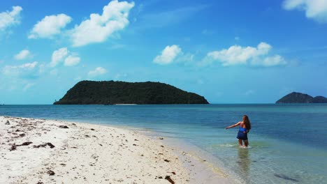 Mädchen,-Das-Ihre-Füße-Auf-Ruhigem-Frischem-Wasser-Der-Seichten-Seelagune,-Exotischer-Strand-Mit-Schönem-Tropischem-Inselhintergrund,-Koh-Pha-Ngan,-Thailand-Wäscht