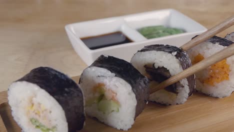 Medium-Slow-Motion-Slider-Shot-of-Taking-a-Piece-of-Sushi-From-a-Wooden-Serving-Board-with-Chopsticks-and-Dipping-into-Soy-Sauce