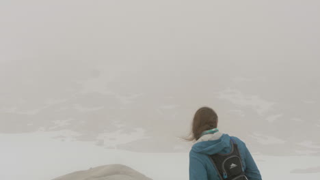 A-Woman-Takes-in-a-View-of-a-Snow,-Desolate,-High-Altitude-Environment-Through-Thick-Fog,-Static-Slow-Motion
