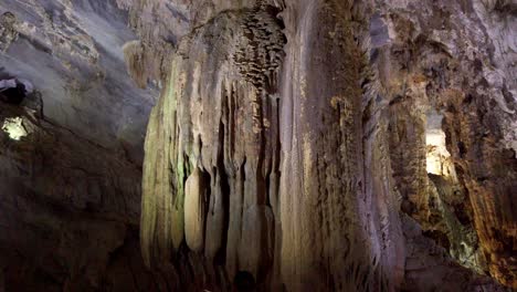 Tourists-look-at-large-Stalagmites-rising-from-the-cave-floor-as-calcium-salts-deposit-over-thousands-of-years,-Walking-tilt-up-shot