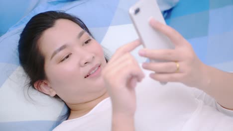 Thailändische-Asiatische-Frau,-Die-Smartphone-Schaut-Und-Berührt,-Entspannen-Sie-Sich-Und-Lächeln-Sie-Mit-Online-sozialen-Medien-Im-Schlafzimmer