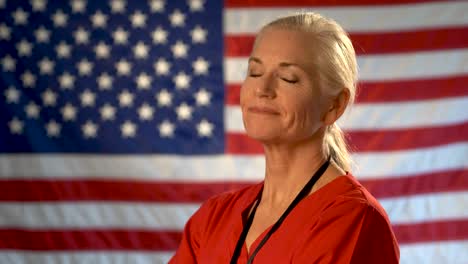 Medium-tight-portrait-of-the-back-of-blonde-nurses-head-as-she-turns-quickly-and-smiles-and-nods-head-yes-with-out-of-focus-American-flag