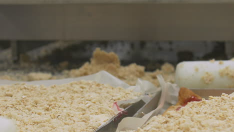 Close-up-of-hands-of-workers-rolling-and-preparing-crumble-mix-on-top-of-a-large-scale-production-baking-tray