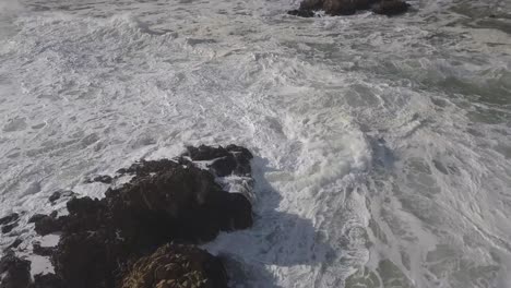 Aerial:-Foamy,-chaotic-ocean-waves-break-in-whitewater-on-shore-rocks