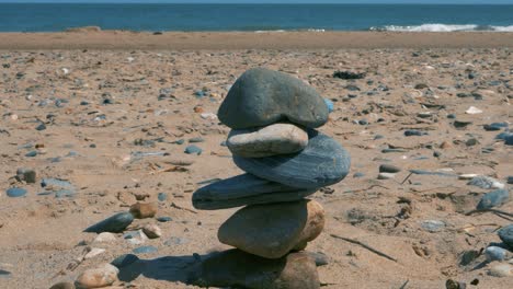 Stone-Balancing-On-Brittas-Bay-Beach,-With-A-Little-Boy-Running-Into-The-Water-On-The-Background-In-County-Wicklow,-Ireland-In-Summer