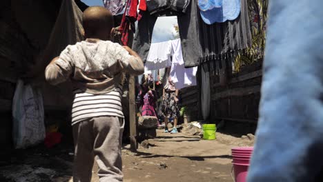 Young-African-kids-childen-walking-through-a-poor-village-slums-while-passing-laundry---following-tracking-shot-180fps-slowmotion