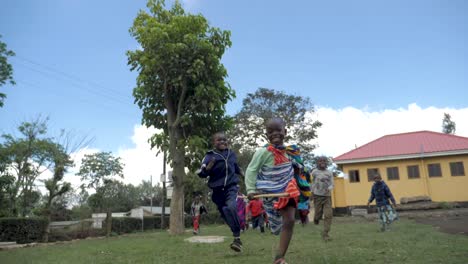 Eine-Gruppe-Lachender-Afrikanischer-Schulkinder,-Die-Auf-Einer-Grünen-Wiese-Auf-Die-Kamera-Zulaufen-Und-Mit-Stöcken-Spielen,-In-Abgelegenen-Dörflichen-Slums-Von-Tansania---180-Fps-Slowmotion