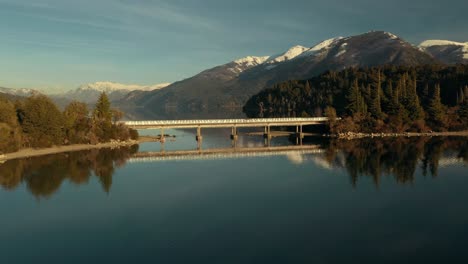 Aerial-shot-orbiting-around-a-bridge-in-the-middle-of-a-scenic-lake-with-mountains-on-background-near-Bariloche-city,-Argentina
