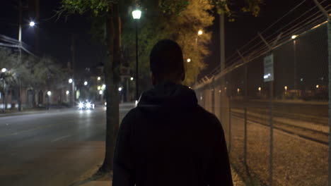 Adolescente-Afroamericano-Camina-Por-La-Calle-Por-La-Noche,-Detrás-De-Medio