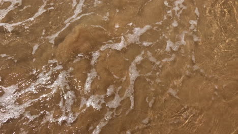 Crystal-clear-transparent-water-splashes-on-shoreline-sandy-beach,-handheld-close-up