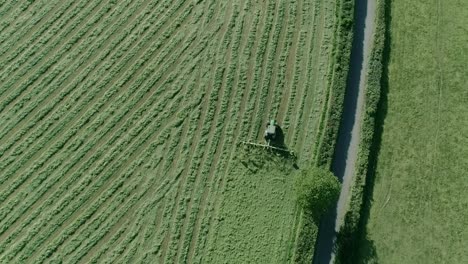 Aerial-of-a-tractor-tedding-alongside-a-hedgerow-and-country-rural-road