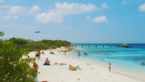 Plane-Flying-Over-The-Beautiful-Te-Amo-Beach-With-Tourists-Enjoying-On-Sunbathing-And-Swimming-In-Bonaire-During-Summer