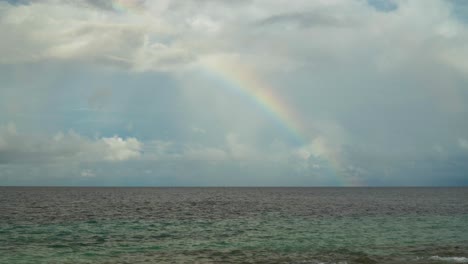 Colorful-quarter-of-a-rainbow-appears-above-the-ocean-with-rain-clouds-behind-it