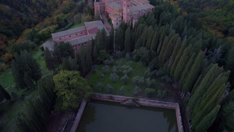 Large-Benedictine-monastery-in-forest-landscape-of-Tuscany,-old-pond,-aerial