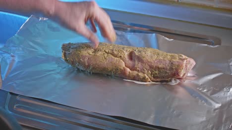A-chef's-white-hand-places-a-tender-marinated-pork-tenderloin-onto-foil-on-a-kitchen-countertop
