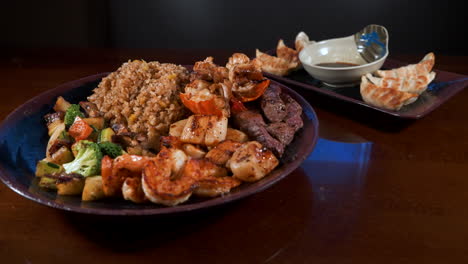 Surf-and-turf-hibachi-dinner-with-dumplings,-shrimp-lobster-steak-scallops-fried-rice-mixed-vegetables-piled-high-on-plate,-slider-4K
