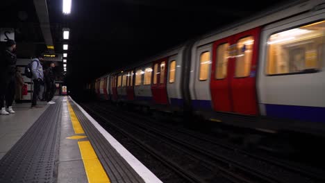 shot-of-a-train-passing-by-in-a-metro-underground-station-full-of-waiting-people-in-London,-United-Kingdom