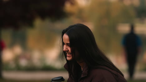 Beautiful-Cheerful-Joyful-Brunette-Girl-Model-Laughing-and-Holding-Coffee-Cup-in-Outdoor-Park,-Blurred-Background