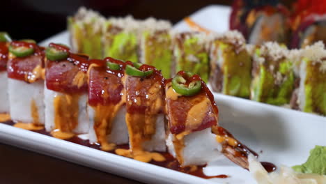 Variety-of-prepared-sushi-rolls,-covered-in-serranos-raw-fish-avocado-tempura-flakes-spicy-mayo-sauce,-slider-close-up-4K