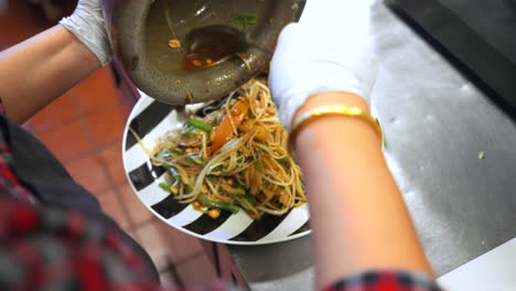 Restaurant-kitchen-staff-plates-sauced-bean-noodle-stir-fry-with-vegetables,-close-up-over-the-shoulder-slow-motion-4K